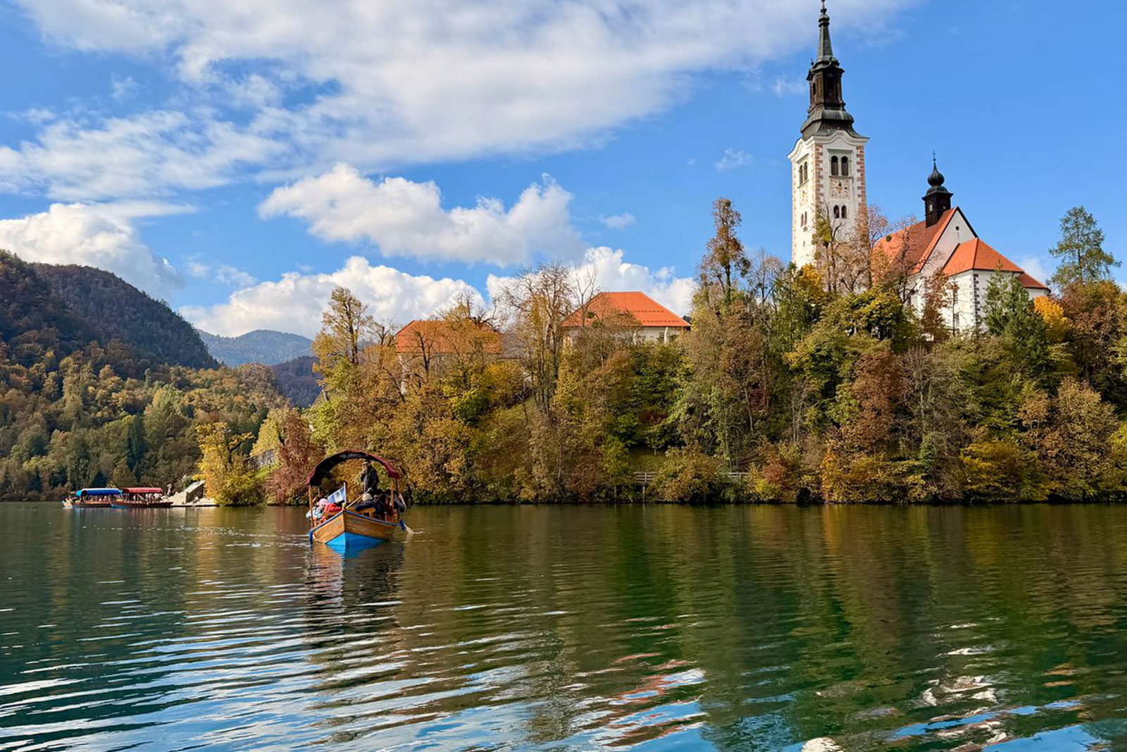 Boat floating in a lake, with a large church building in the background, behind orange trees