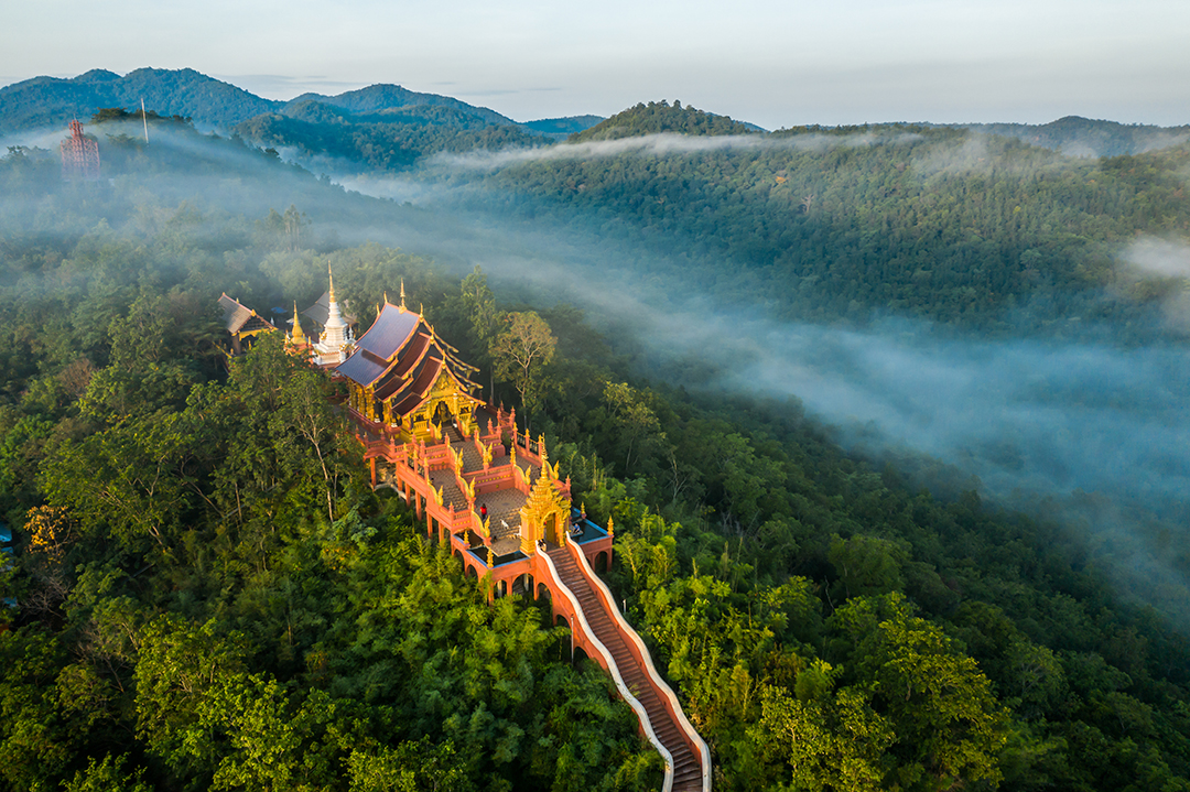 Large Thai temple at the top of a mountain, surrounded by thick forrest