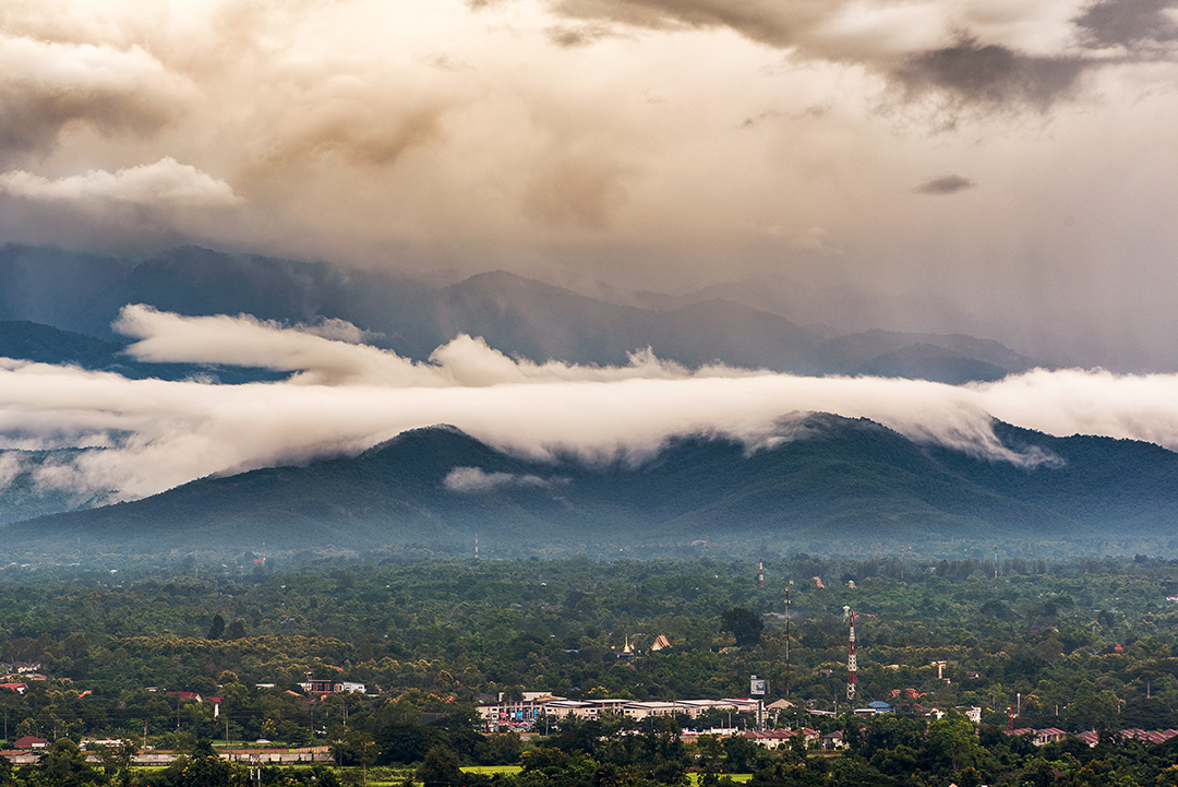 Wide view shot of Chiang Mai, with a town and large clouds in the distance