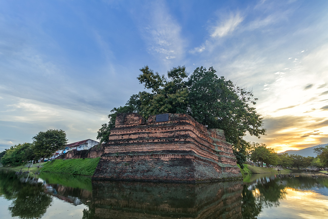 Lake with rustic buildings on top, with the sunset in the distance