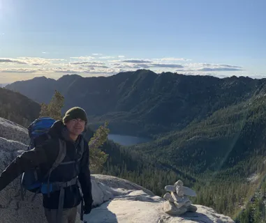 Image of a trip prep specialist on a mountain top. A lake and mountain range can be seen on the horizon.