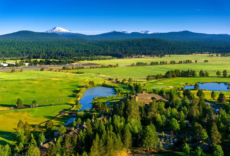 Wide shot of green pasture, large house in foreground, mountains in background.