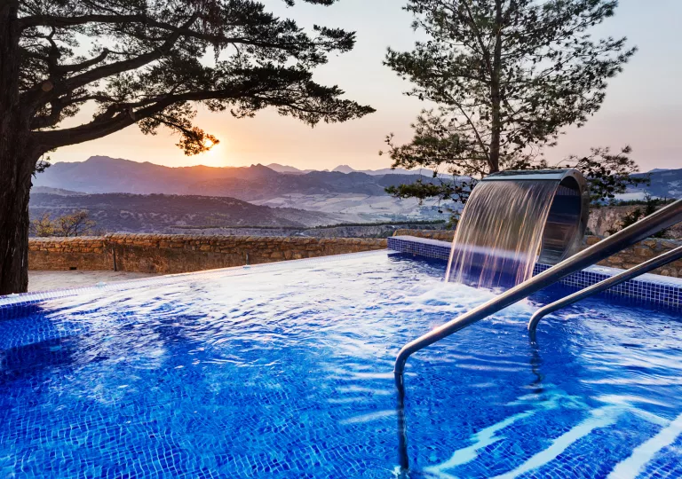 Outdoor pool with a fountain on the right, looking out to large mountains in the distance