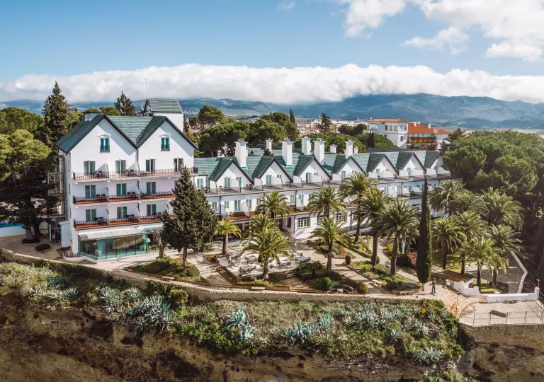 Exterior wide view of white and blue hotel buildings with palm trees in the front