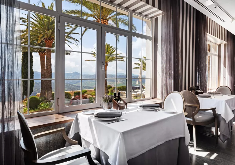 Dining table with white and gray table cloths, next to a large window