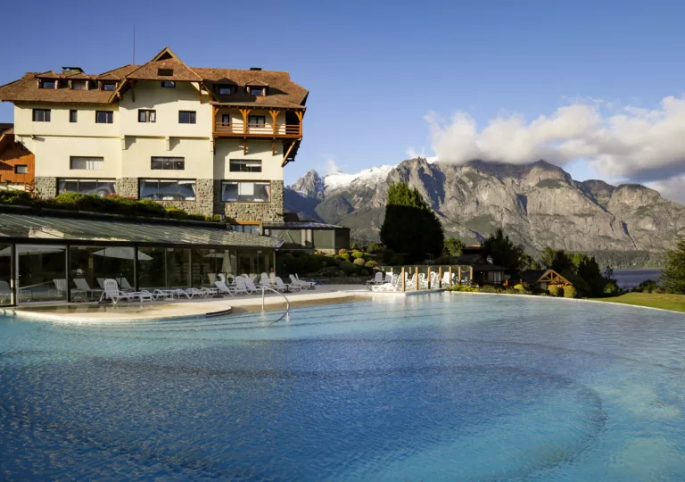 Outdoor pool with white chairs and a white building and large mountains in the background