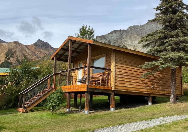 Wooden cabin with a small staircase in front and wooden chairs on the porch