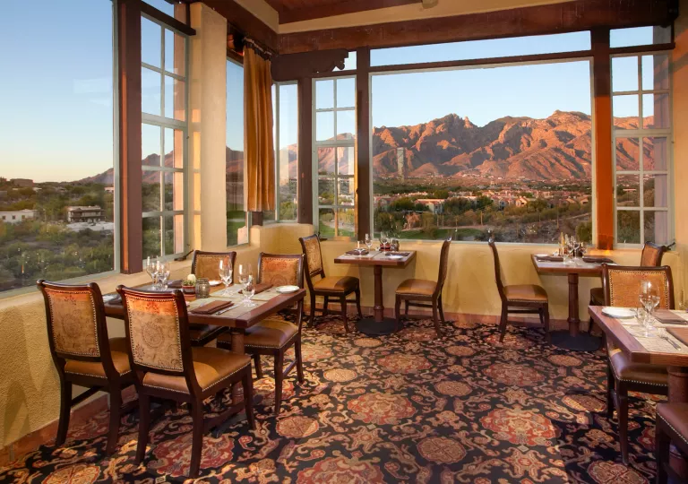 Indoor dining area, covered with carpet and cushioned chairs, looking out to mountains
