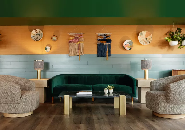 Indoor lounge with a green sofa and tan, cushioned chairs and décor on the wall