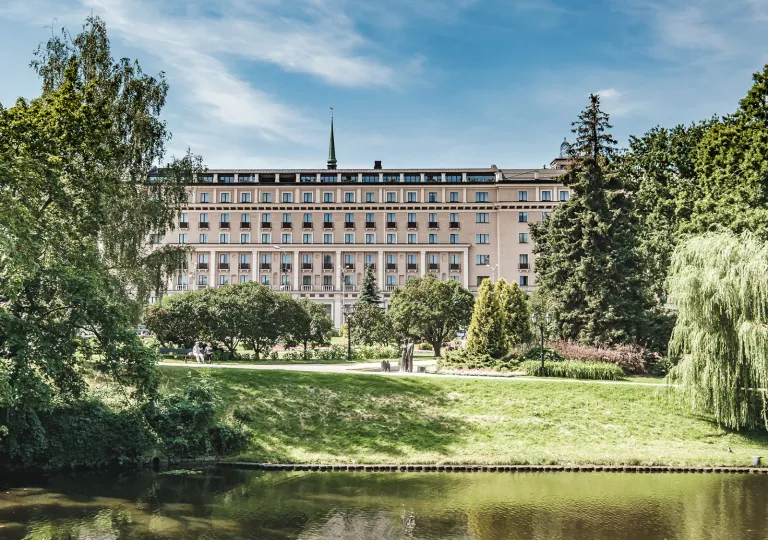 Large building with 4 stories of windows with an outdoor grass area and a small pond