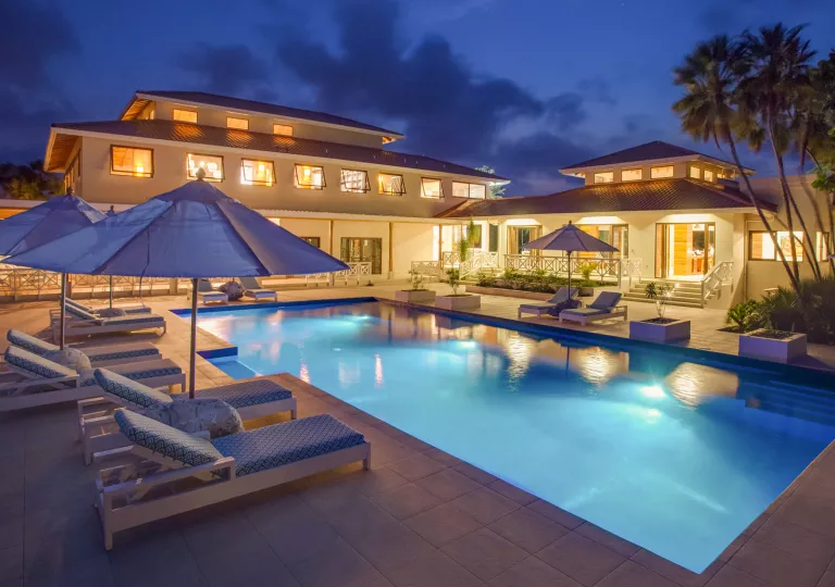 Outdoor pool with blue reclining chars with an illuminated building in the back