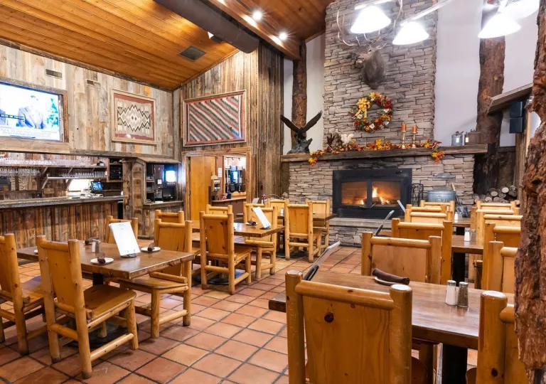 Indoor dining area in a lodge-style hall, with a stone fireplace in the background