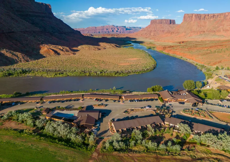 Multiple brown building next to a large canyon valley with a river in the background