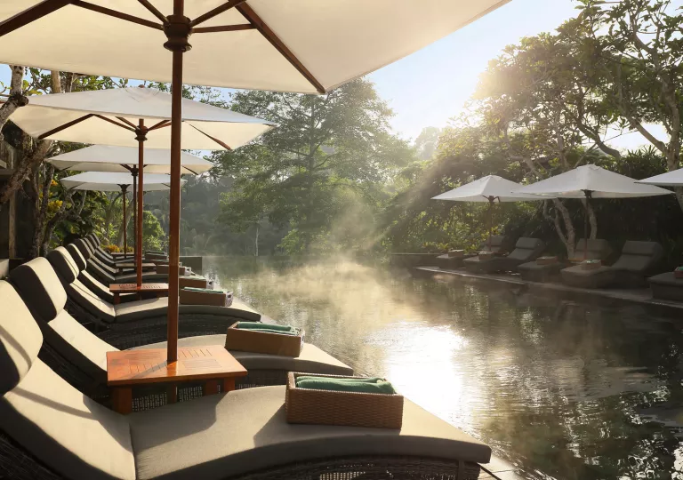 Outdoor pool surrounded by reclining chairs, white smoke on the water