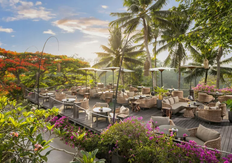Outdoor patio with cushioned chairs and umbrellas, looking out to the sunset and a smoky forest