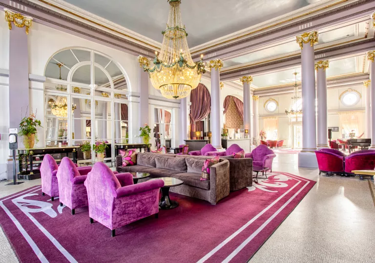 Hotel seating area with pink and gray velvet chairs and a large chandelier