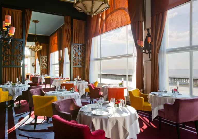 Dining hall with red and yellow cushioned chairs, and large windows with orange curtains