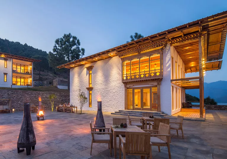 White building with a wooden balcony and outdoor patio area with tables and chairs