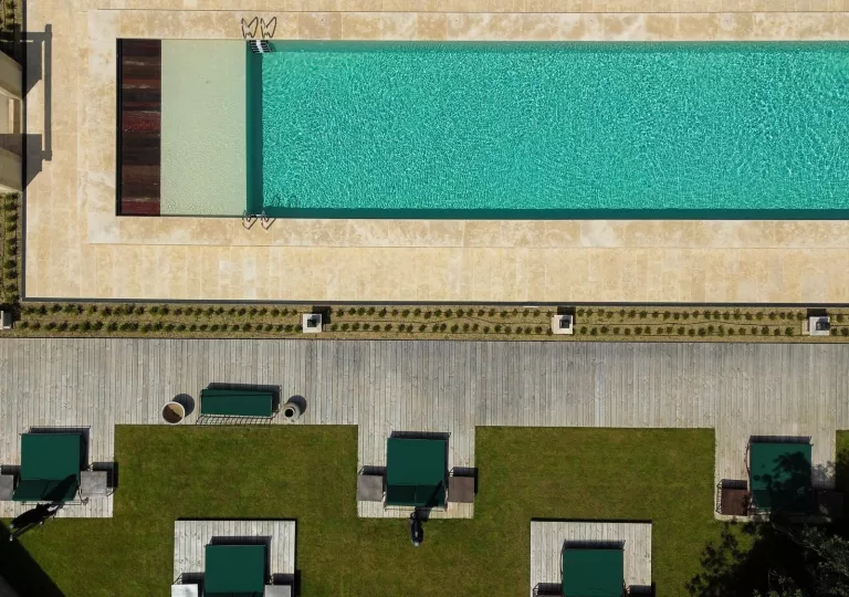 Sky view of an outdoor pool with green pool chairs and grass areas surrounding the pool