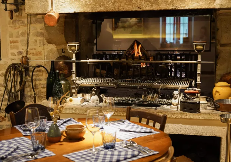 Indoor dining area with a table in front of an open grill and fire pit