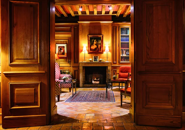Library with large wooden doors, and a painting of a woman above a stone fireplace
