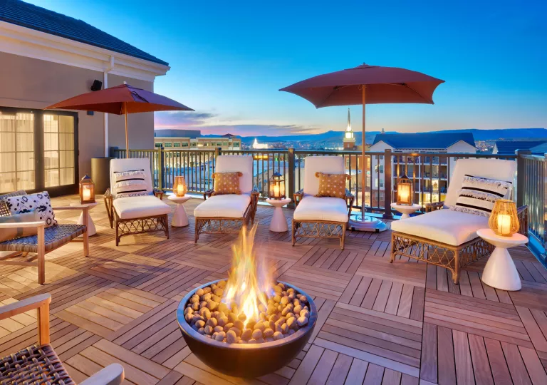 Wooden balcony with white chairs surrounding a stone firepit