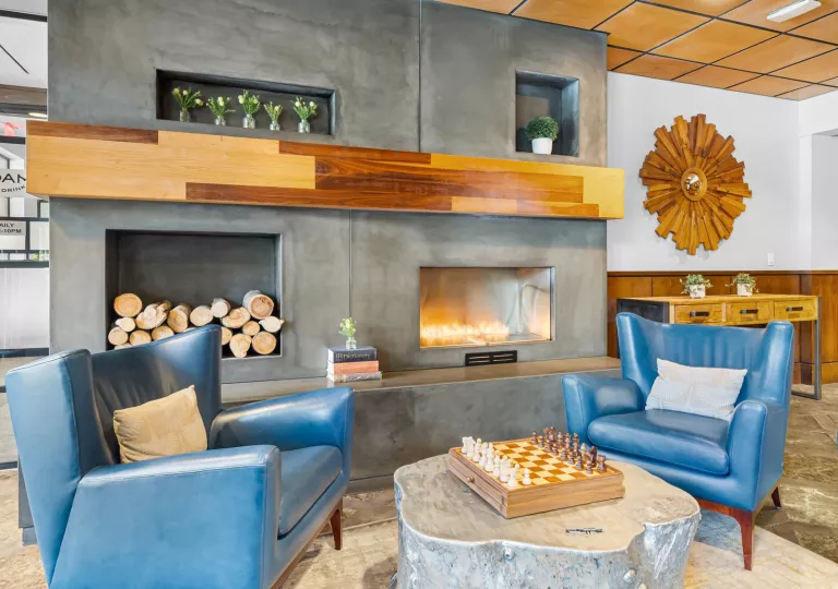 Lounge area in front of a fireplace wit blue chairs and a chess board on a table
