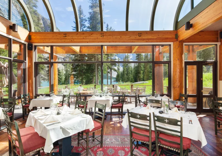 Indoor dining area surrounded by glass walls, looking out to a lake surrounded by trees