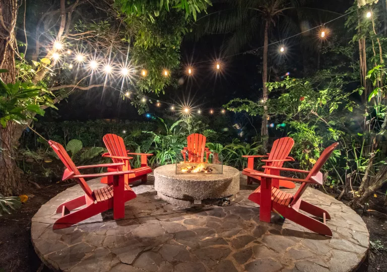 Red lawn chairs surrounding a stone fire pit outdoors on a circular rock slab