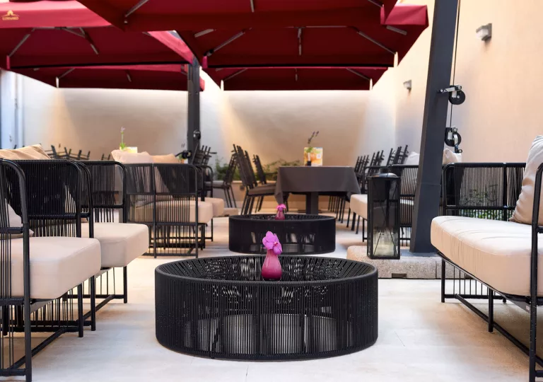 Outdoor lounge area with black, woven chairs and dining tables in the background