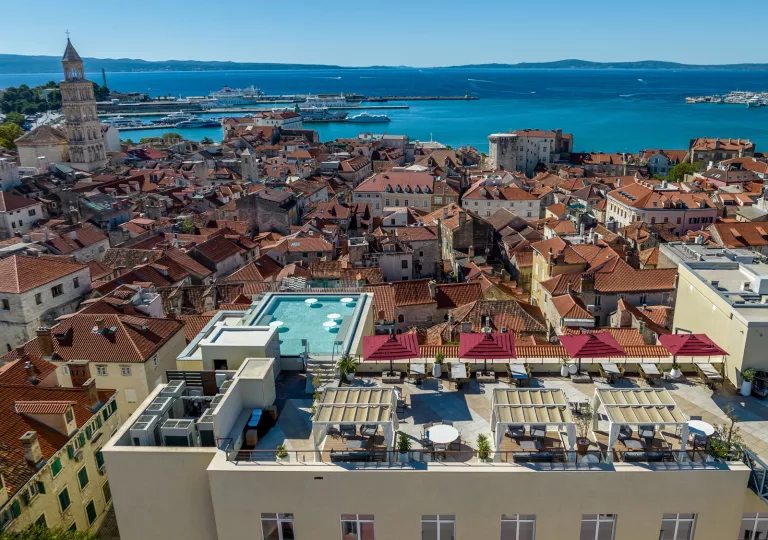 Sky view of yellow buildings with orange roofs, with a building having a pool on the roof