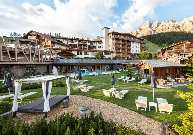 Exterior view of large, lodge-style hotel buildings with an outdoor pool and reclining lawn chairs