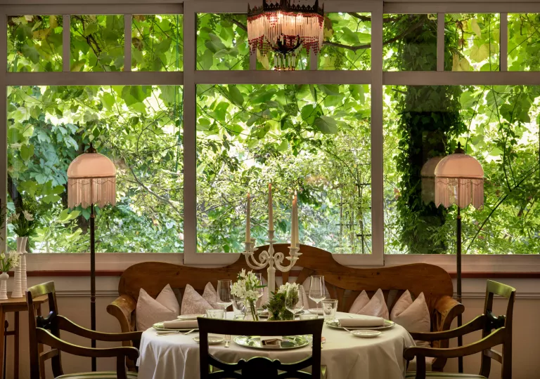 dining table under chandelier next to big windows with view of greenery