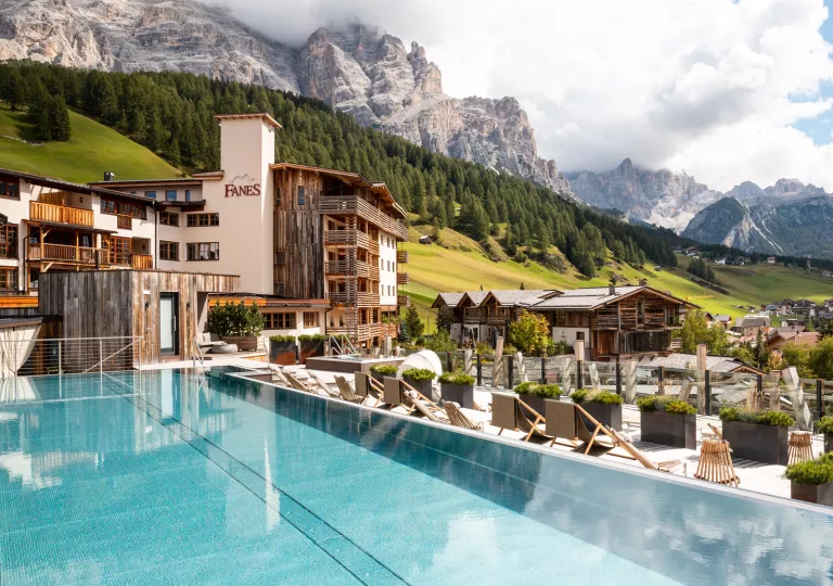 Outdoor infinity pool overlooking a hotel complex and tall, tree-covered hills