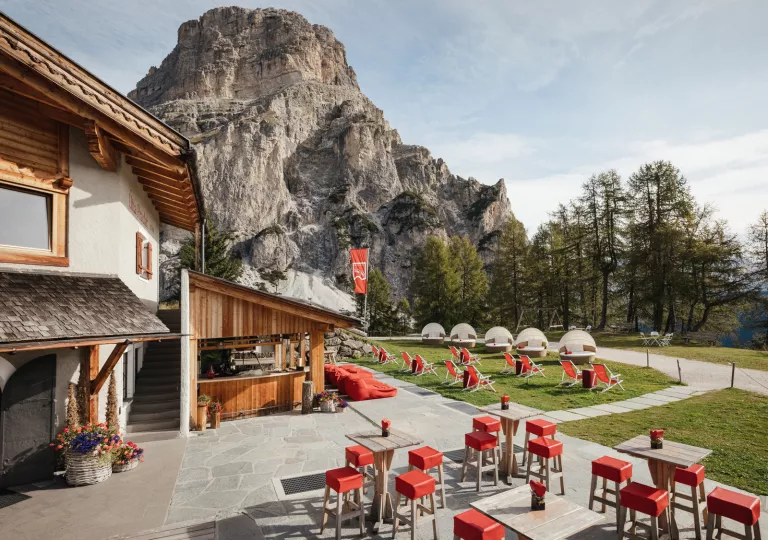 Stone and wood lodge with red chairs outside and a large mountain in the background