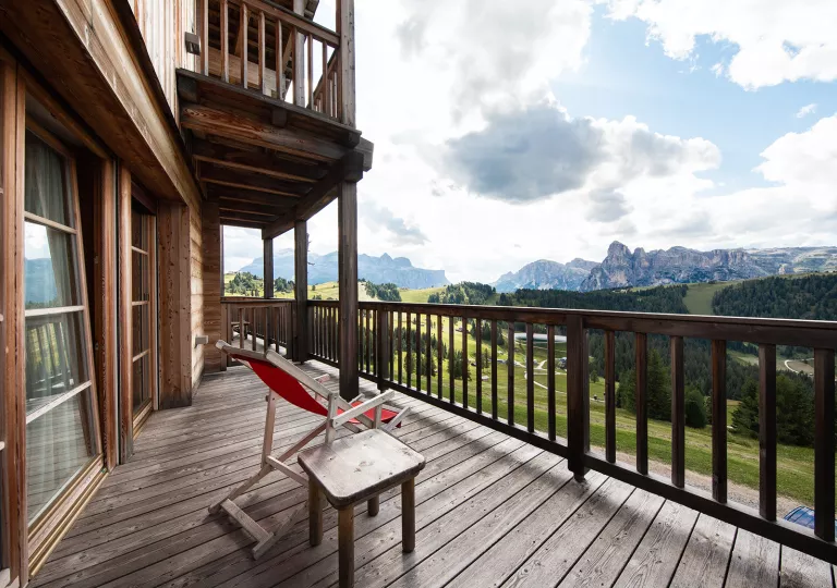 Wooden balcony with a red chair looking out towards cloud-covered mountains