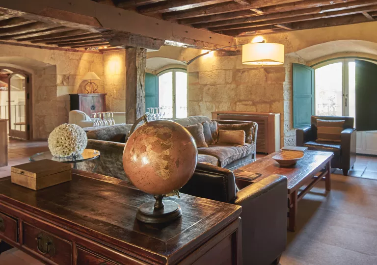 Indoor lounge with large, wooden pillars and wooden furniture, with a globe on the coffee table