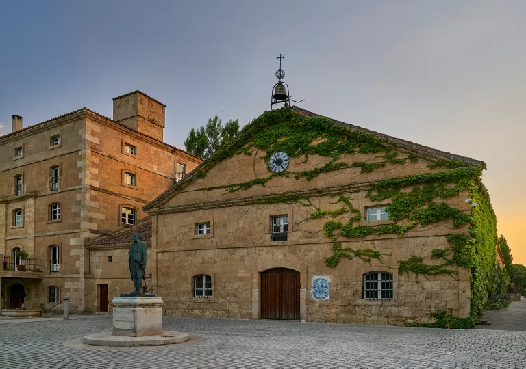 Exterior view of stone building covered in plants, with a bell on top