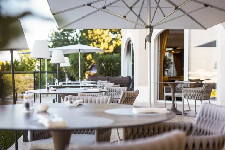 Outdoor eating area with tan cushioned chairs and umbrellas