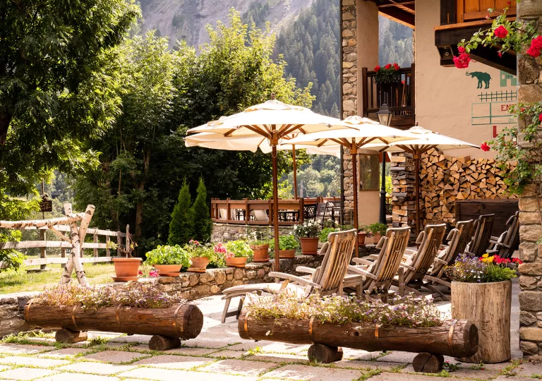 Outdoor patio with umbrellas and wooden chairs looking out to a garden