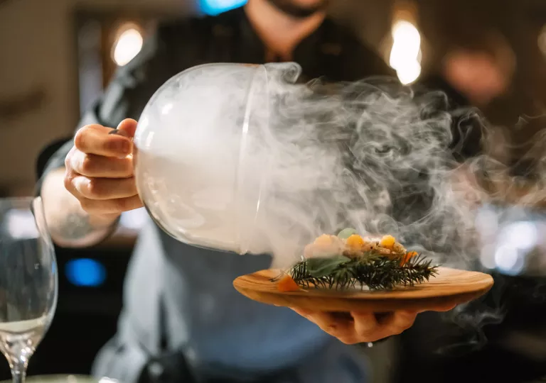 Man holding a plate of food while holding a dome of fog over the plate