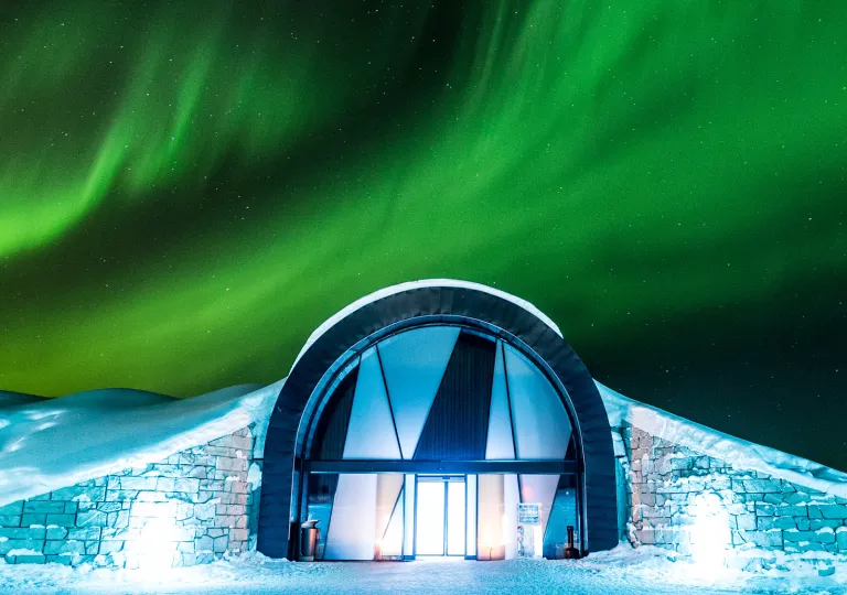 Entrance of building in the middle of a snow valley, with the Northern Lights in the sky