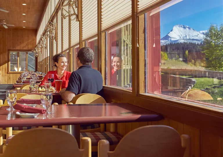 Man and woman at a dining table staring out a window towards mountains and a forest