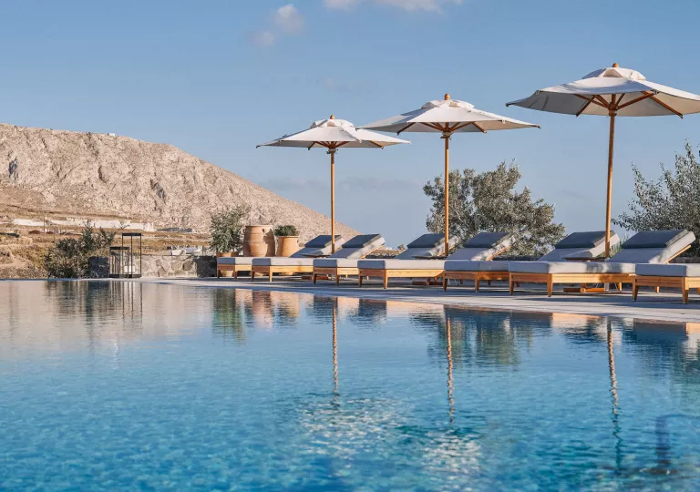 Outdoor pool surrounded by chairs and umbrellas, with a mountain in the background
