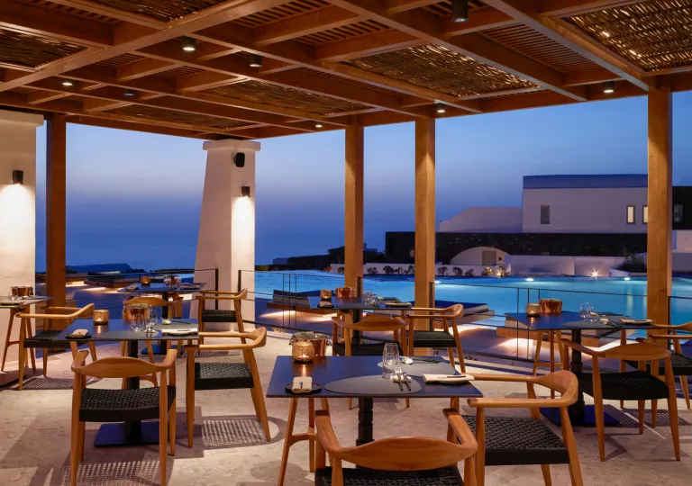 Outdoor dining area with candles on each table and a view of an infinity pool