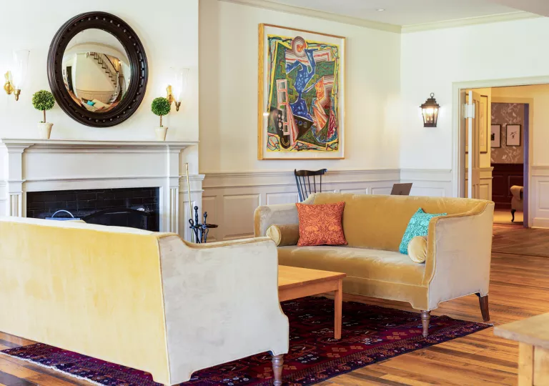 Tan, velvet sofas in front of a stone fireplace with a large mirror above