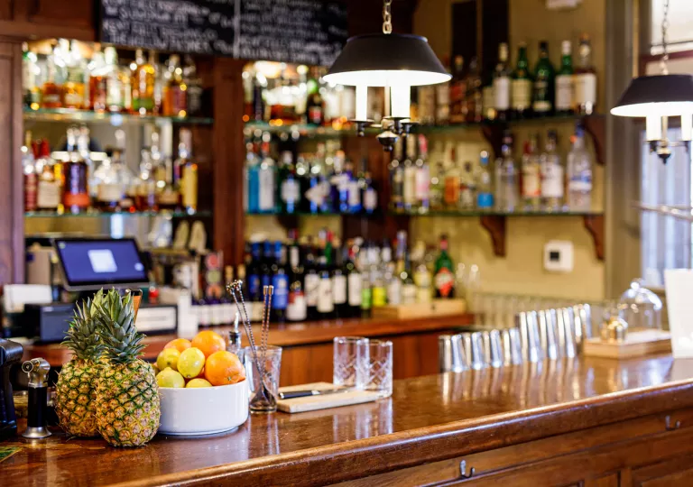Wooden bar counter top with glasses, fruit and bottles of liquor in the background