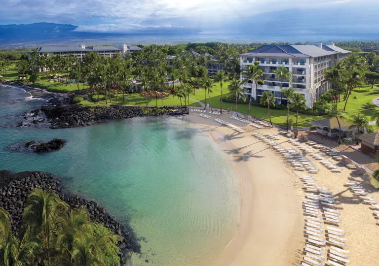 Pool chairs lined up by the coast of the ocean with a large hotel building in the background