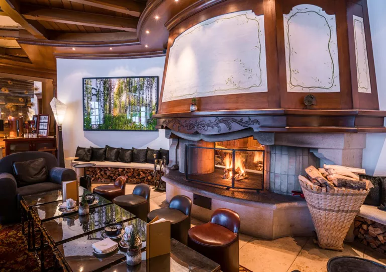 Indoor lounge with cushioned stools around a table with a fireplace behind