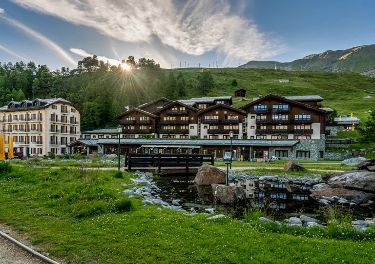 Brown hotel building with a small river and pond, with a wooden bridge in front